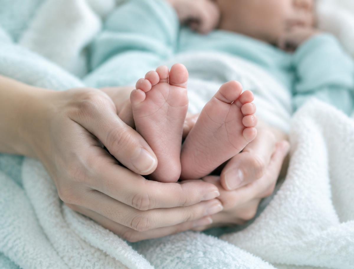 A mother's hands gently holding her newborn's feet